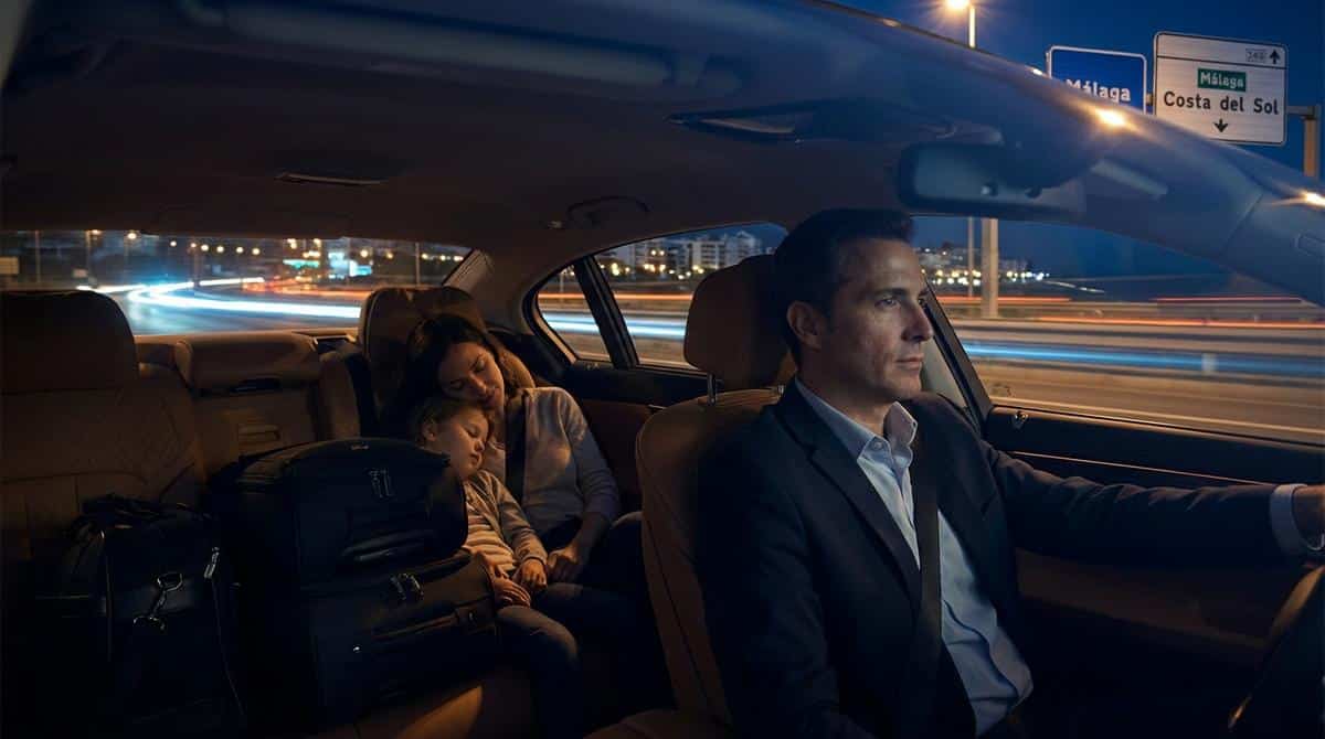 Interior de un coche de transfer privado de noche con un chófer conduciendo y una familia descansando en los asientos traseros.